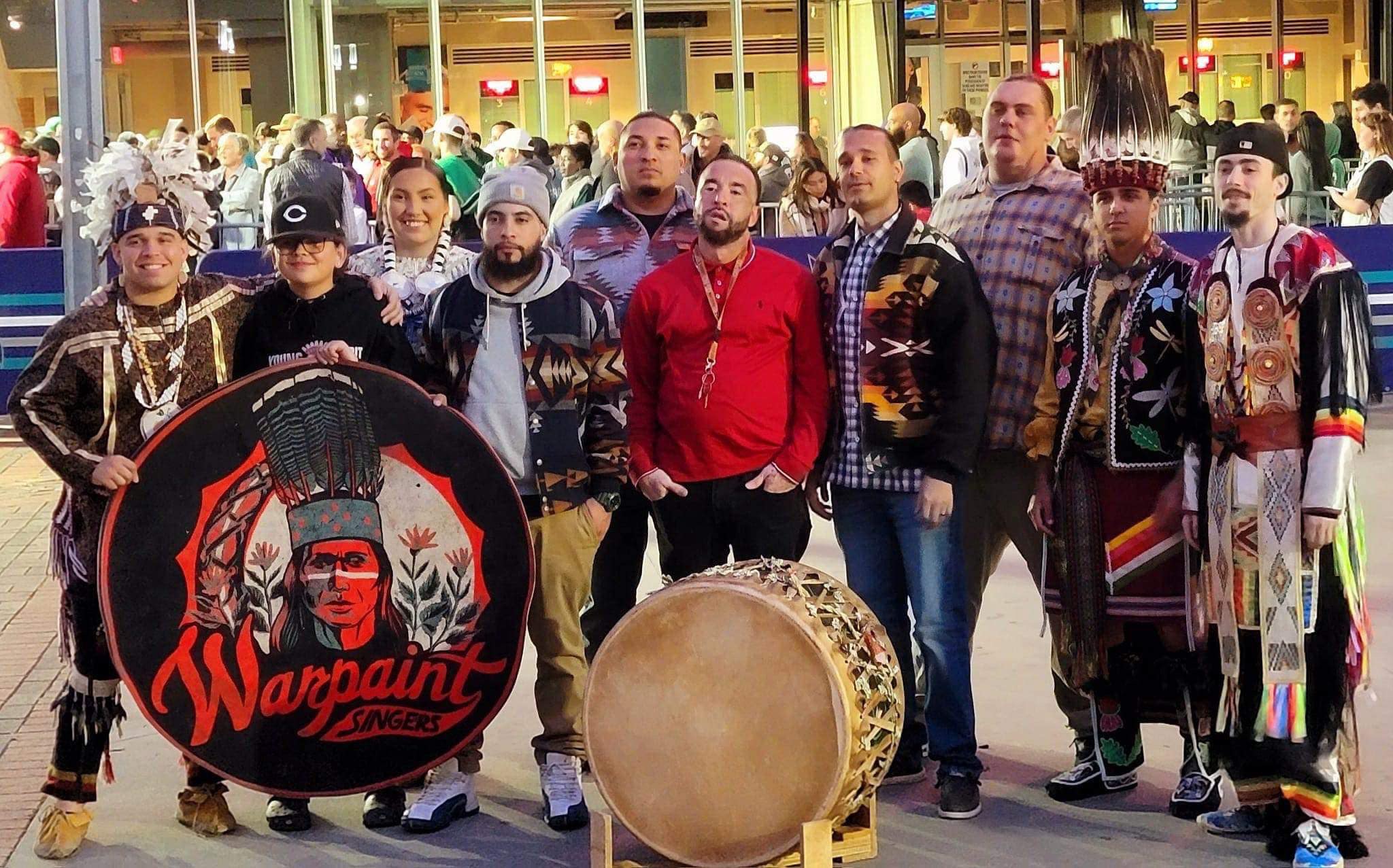 Native Americans, some in traditional dress, with a drum and a banner for WarPaint Singers.